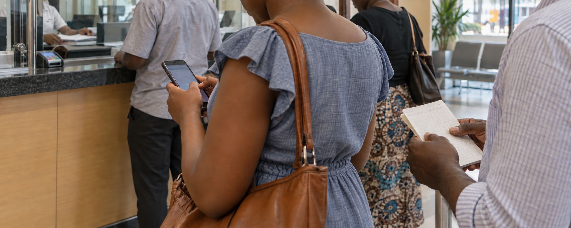 Scène illustrée : une personne consulte son téléphone devant un guichet bancaire, tandis qu'une autre tient un carnet.